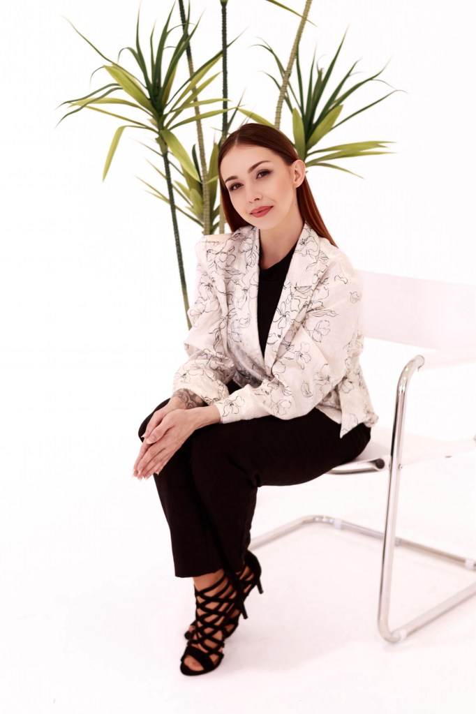 Sharissa is sitting in a chair with a white background and green plant behind her.